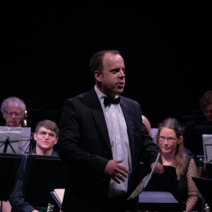 Michael Cox speaks to the audience with band members behind him